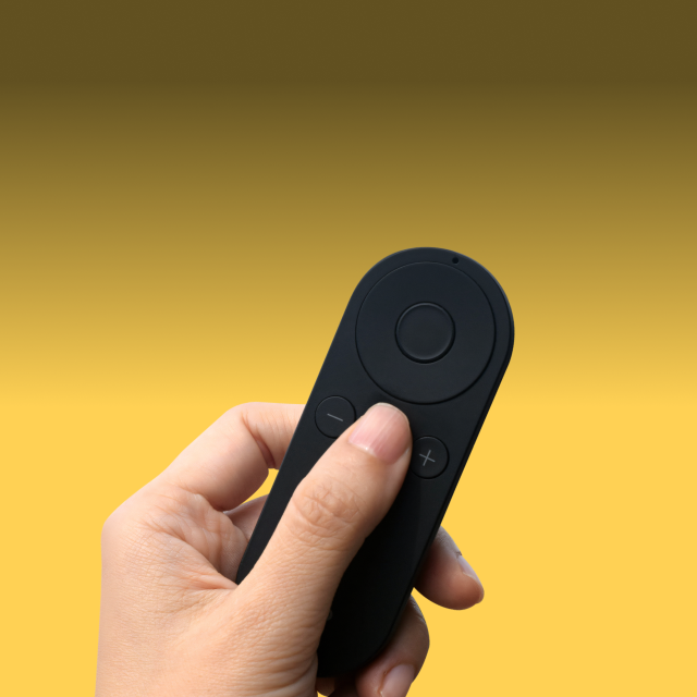 Hand holding a compact lightweight remote control for Pivo Pods and Max with buttons for rotation and shutter functions against a yellow background